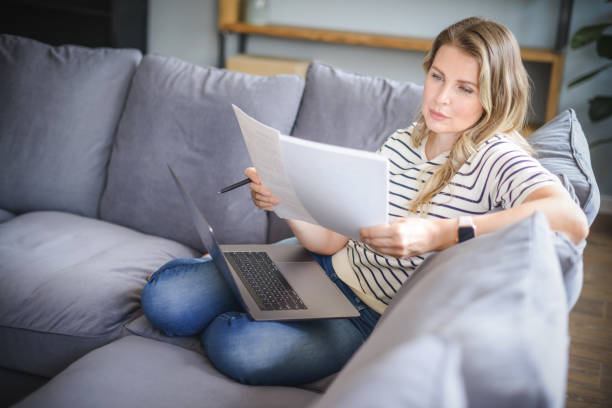 istock attractive middle aged woman sitting on the couch( laptop, paperwork) 1318025782