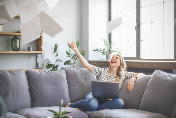 istock attractive middle aged woman sitting on the couch( laptop, paperwork, throwing) 1318028020