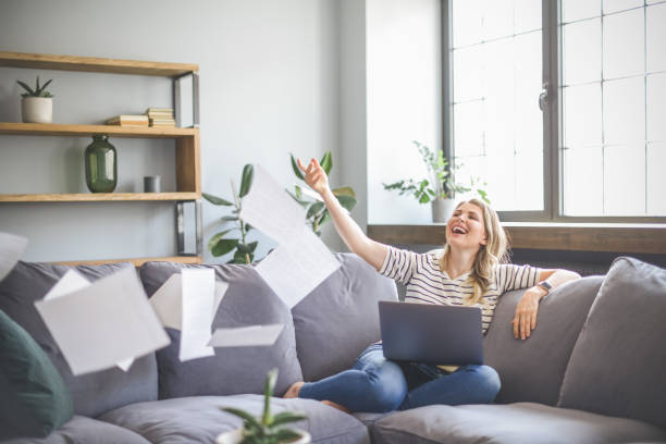 istock attractive middle aged woman sitting on the couch( laptop, paperwork, throwing) 1318029003