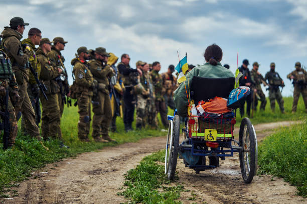 um homem deficiente em uma cadeira de rodas contra o fundo de um grupo de soldados - conciliator - fotografias e filmes do acervo