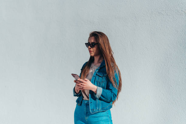 istock Woman using a smartphone while standing in front of a white wall 1318032090