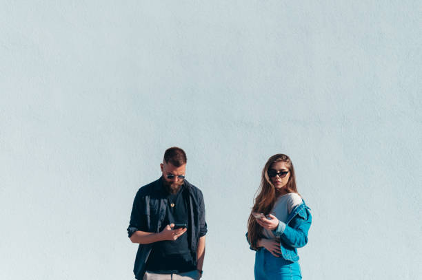 istock Couple using smartphones while standing in front of a white wall 1318032165