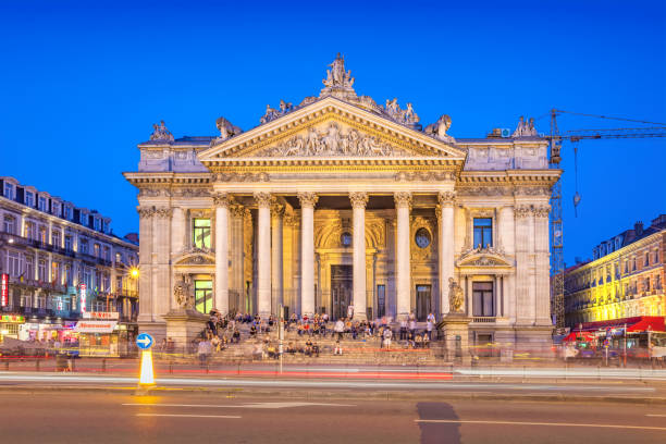 People sit on the steps of the Brussels Stock Exchange (Bourse de Bruxelles) in downtown Brussels Belgium in the evening.