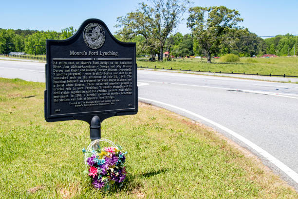 un panier de fleurs se trouve au pied d’un marqueur historique en bordure de route pointant vers le site du lynchage de quatre afro-américains par une foule démasquée sur juillet 25, 1946, près de la moore"u2019s ford bridge dans le comté de walton, - unmasked photos et images de collection