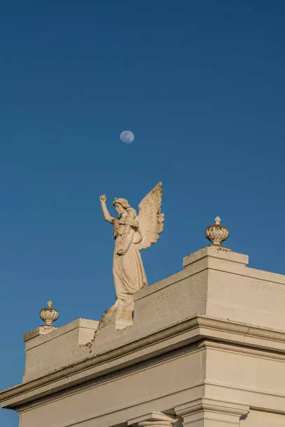 A  beautiful angel atop a crypt under a full moon on blue sky