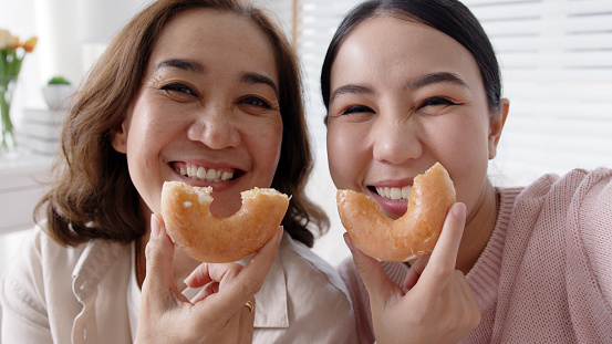 Portrait attractive beautiful two people family use cellphone take photo picture doughnut video story smiley overjoy donut at sofa couch living room have good time together quarantine social distance.