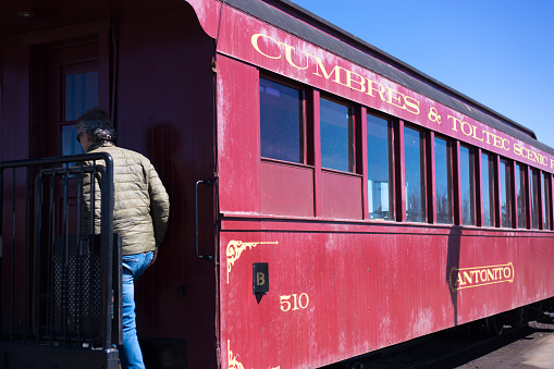 Antonito, CO: A man boards an old-fashioned red car of the Cumbres & Toltec Scenic Railroad. The Victorian steam train is a popular tourist attraction and travels 64 miles from Antonito, CO to Chama, NM and back. It has been designated a national historic landmark.