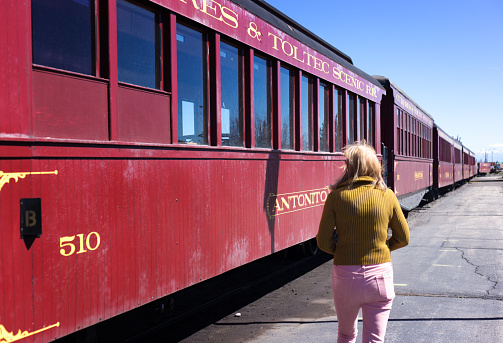 Antonito, CO: A woman walks past the old-fashioned red cars of the Cumbres & Toltec Scenic Railroad. The Victorian steam train is a popular tourist attraction and travels 64 miles from Antonito, CO to Chama, NM and back. It has been designated a national historic landmark.