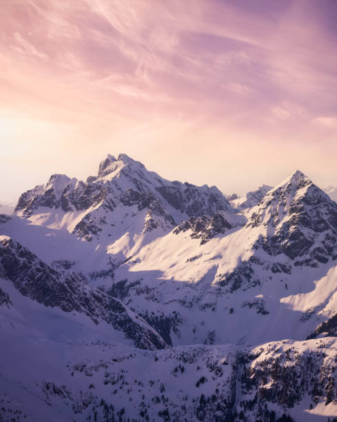 Snow Covered Canadian Mountain Landscape Aerial View from Airplane of Blue Snow Covered Canadian Mountain Landscape in Winter. Colorful Pink Sky Art Render. Tantalus Range near Squamish, North of Vancouver, British Columbia, Canada. snow sunset winter mountain stock pictures, royalty-free photos & images
