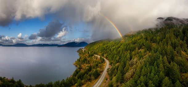 Aerial panoramic view of the Sea to Sky Highway in Howe Sound, North of Vancouver, British Columbia, Canada. Colorful Cloudy Sky with Rainbow Art Render.