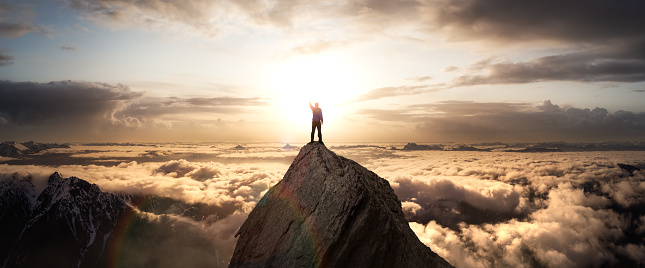 Magical Fantasy Adventure Composite of Man Hiking on top of a rocky mountain peak. Background Landscape from British Columbia, Canada. Sunrise Dramatic Colorful Sky
