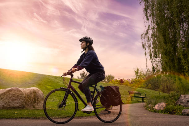 Adventure Woman Bike Riding in a Park Adult Caucasian Woman Riding a Bicycle on a path in a modern city park. Sunset Art Render. Taken in Hawthorne Rotary Park, Surrey, Vancouver, British Columbia, Canada. surrey british columbia stock pictures, royalty-free photos & images