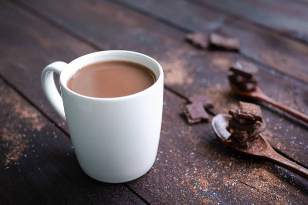 chocolate milk in white cup with bar chocolate in spoon on wooden table background. - hot chocolate imagens e fotografias de stock