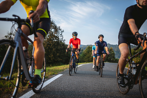 Low angle personal perspective of male and female road bike riders in 20s and 30s approaching and moving past camera during workout.