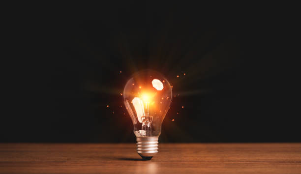 istock Orange light glowing from light bulb on wooden table with background, creative ideas and innovation concept. 1318070055