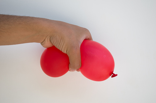 hand squeezing red water filled balloon and white isolated background.