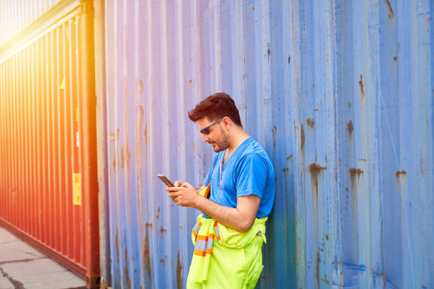 istock Foreman in casual suite chats with mobile phone in container site when breaking time and stand laying the blue box 1318091941