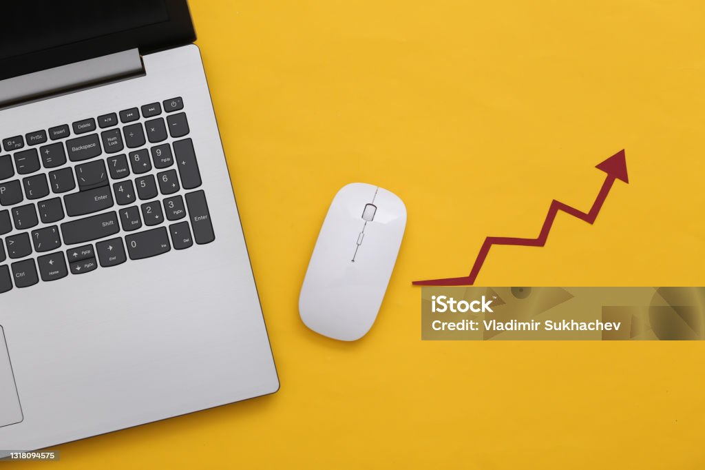 Laptop and pc mouse with a rising arrow on yellow background. Online business, trading. Top view. Flat lay Computer Mouse Stock Photo