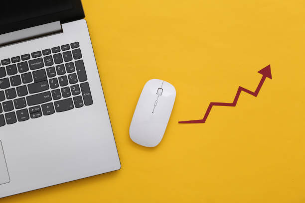 Laptop and pc mouse with a rising arrow on yellow background. Online business, trading. Top view. Flat lay stock photo