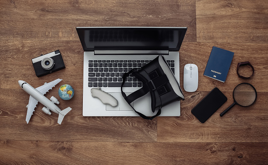 Flat lay composition of laptop and vr headset, travel accessories on a wooden floor. Virtual Tourism. Top view.