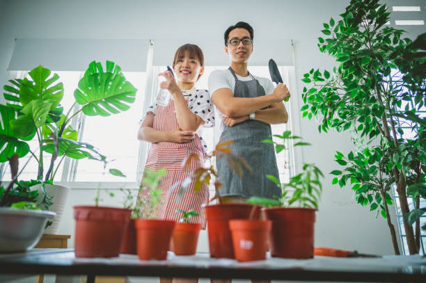 istock Happy Asian young couple holding with potted plants and tools looking at camera 1318097043