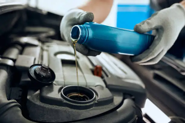 Close- up of mechanic pouring motor oil while doing car maintenance at auto repair shop.