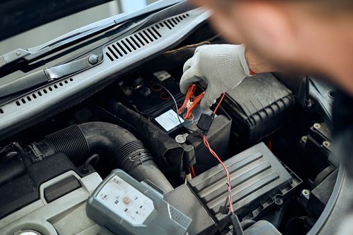 Close-up of auto mechanic attaching jumper cables while checking car battery in a repair shop.