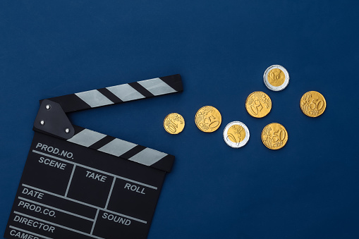 Movie clapper board and coins on classic blue background. Cinema fees. Filmmaking, Movie production. Top view