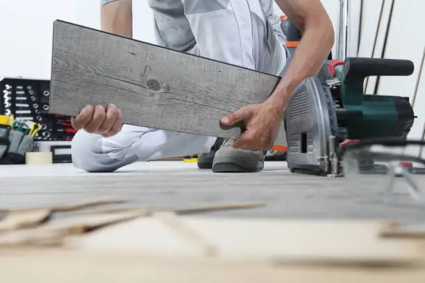 Photo of Worker hands installing timber laminate vinyl floor. Wooden floors house renovation.
