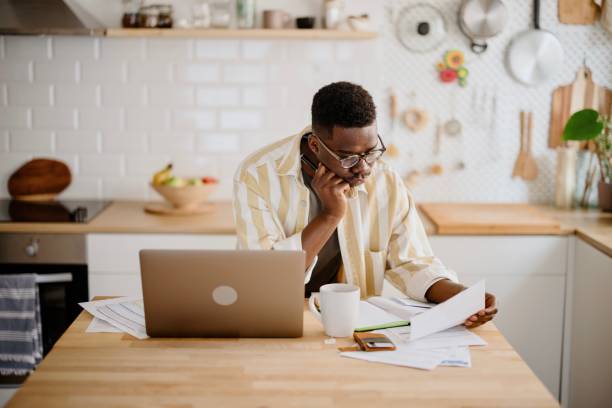 istock Young African man sits in kitchen while using laptop to work remotely from his home 1318114502
