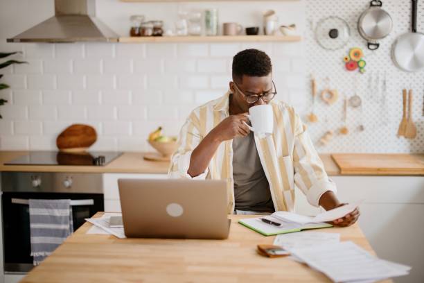 istock Young African man sits in kitchen while using laptop to work remotely from his home 1318114570