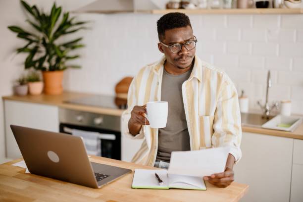 istock Young African man sits in kitchen while using laptop to work remotely from his home 1318114595