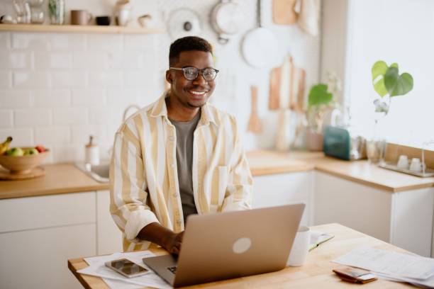 istock Young African man sits in kitchen while using laptop to work remotely from his home 1318114641