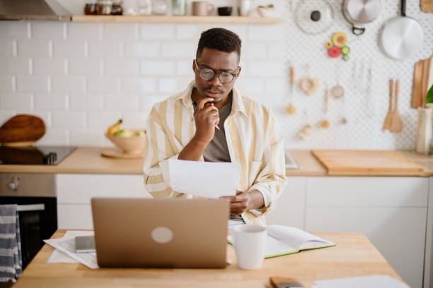 istock Young African man sits in kitchen while using laptop to work remotely from his home 1318114669