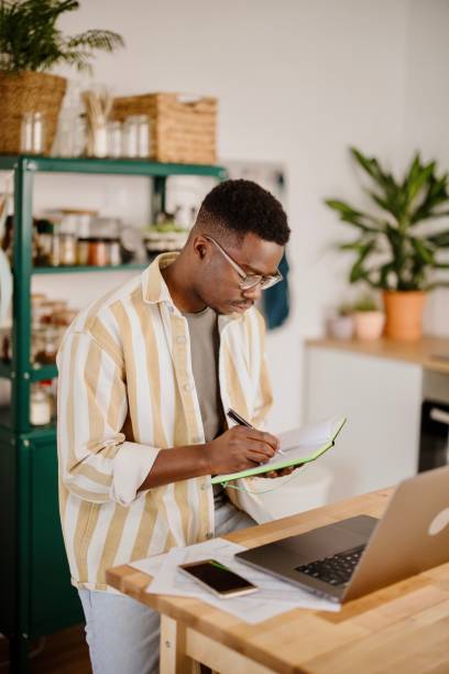 istock Young African man sits in kitchen while using laptop to work remotely from his home 1318114697
