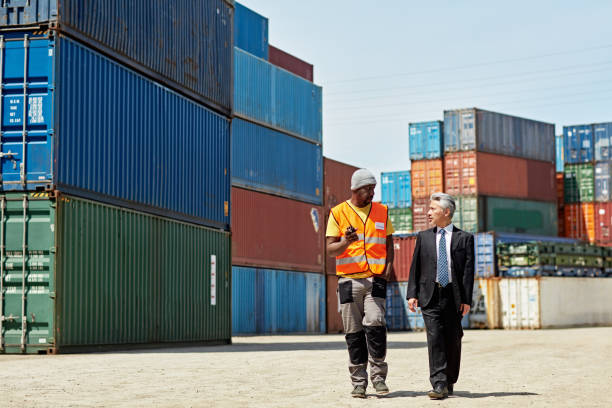 Full length front view of Black and Japanese coworkers in 40s and 50s approaching camera as they discuss logistics in container terminal.