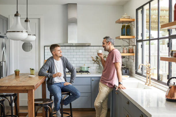 Happy gay couple at home Happy homosexual couple talking at home. Smiling gay men are having coffee. They are in kitchen. gay dinner table stock pictures, royalty-free photos & images
