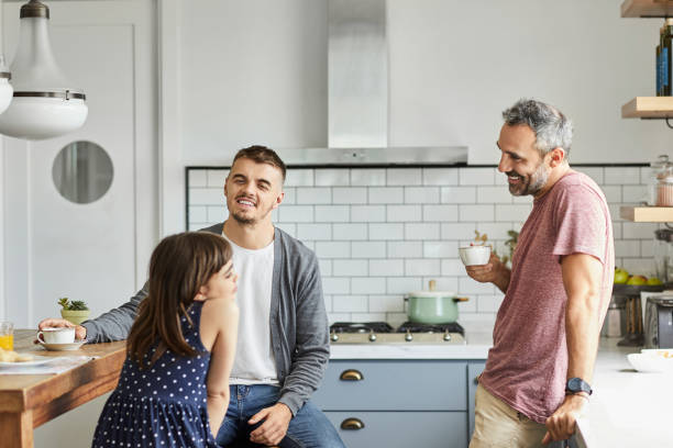 Smiling gay couple with daughter at home Girl talking with parents at home. Gay couple is having coffee with daughter. They are in kitchen. gay dinner table stock pictures, royalty-free photos & images