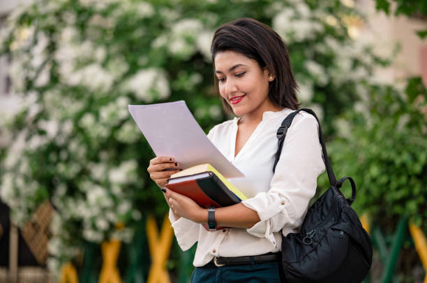 jeune étudiant féminin retenant des livres et vérifiant ses papiers de note - indian girls audio photos et images de collection