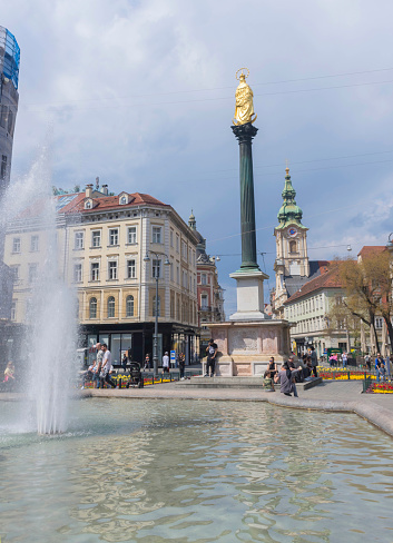 Graz, Austria-April 25, 2021: people relaxing near Mary's Column and fountain in Jakominiplatz Square in the city center of Graz, Styria region, Austria, in sunny spring day.