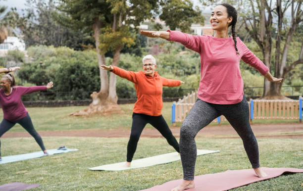 personas multigeneracionales haciendo yoga de mantenimiento de clases en el parque de la ciudad - concéntrate en la cara de la chica correcta - women yoga yoga class mature adult fotografías e imágenes de stock