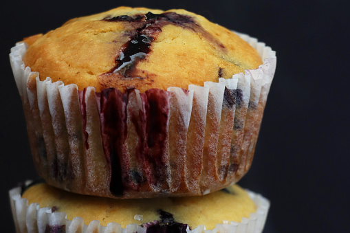 Stock photo showing close-up view of a pile homemade blueberry muffins in paper cake cases against a dark background.