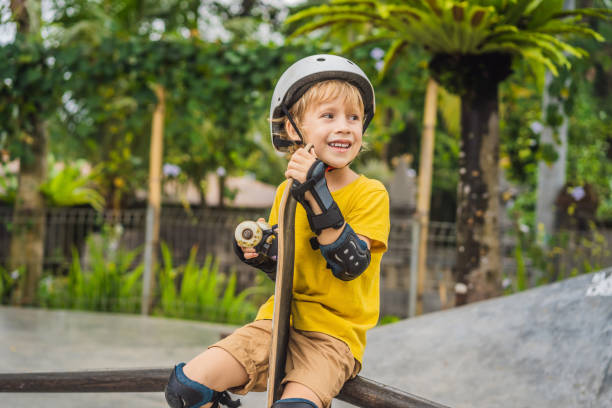 Athletic boy in helmet and knee pads learns to skateboard with in a skate park. Children education, sports stock photo