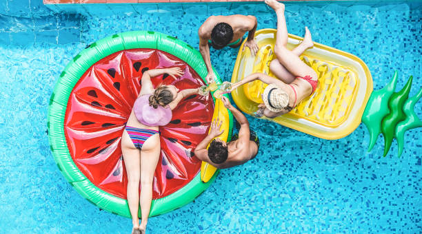 istock Happy friends having fun inside swimming pool during summer vacation - Focus on hands holding cocktails 1318130988