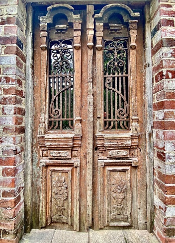 Vertical still life of aged carved tan wooden house doors with metal over glass and modern brick surrounding wall