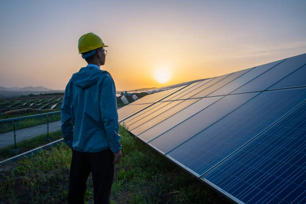 ingenieur steht in solarkraftwerk und schaut auf sonnenaufgang - solar panel fotos stock-fotos und bilder