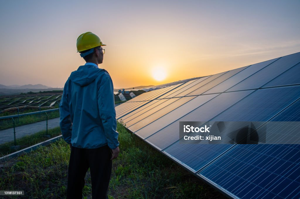 Engineer standing in solar power station looking sunrise Solar Panel Stock Photo