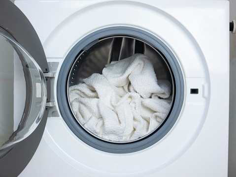 Wash white clothes. White towels inside the open washing machine. Sanitize the laundry.