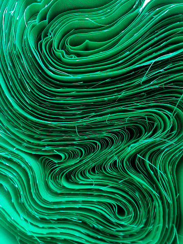 abstract background of cotton fabric rolls. wavy bundles of green fabric edges