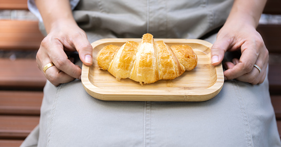 The woman's hand was picking up the croissant that had been placed on a wooden tray in her lap